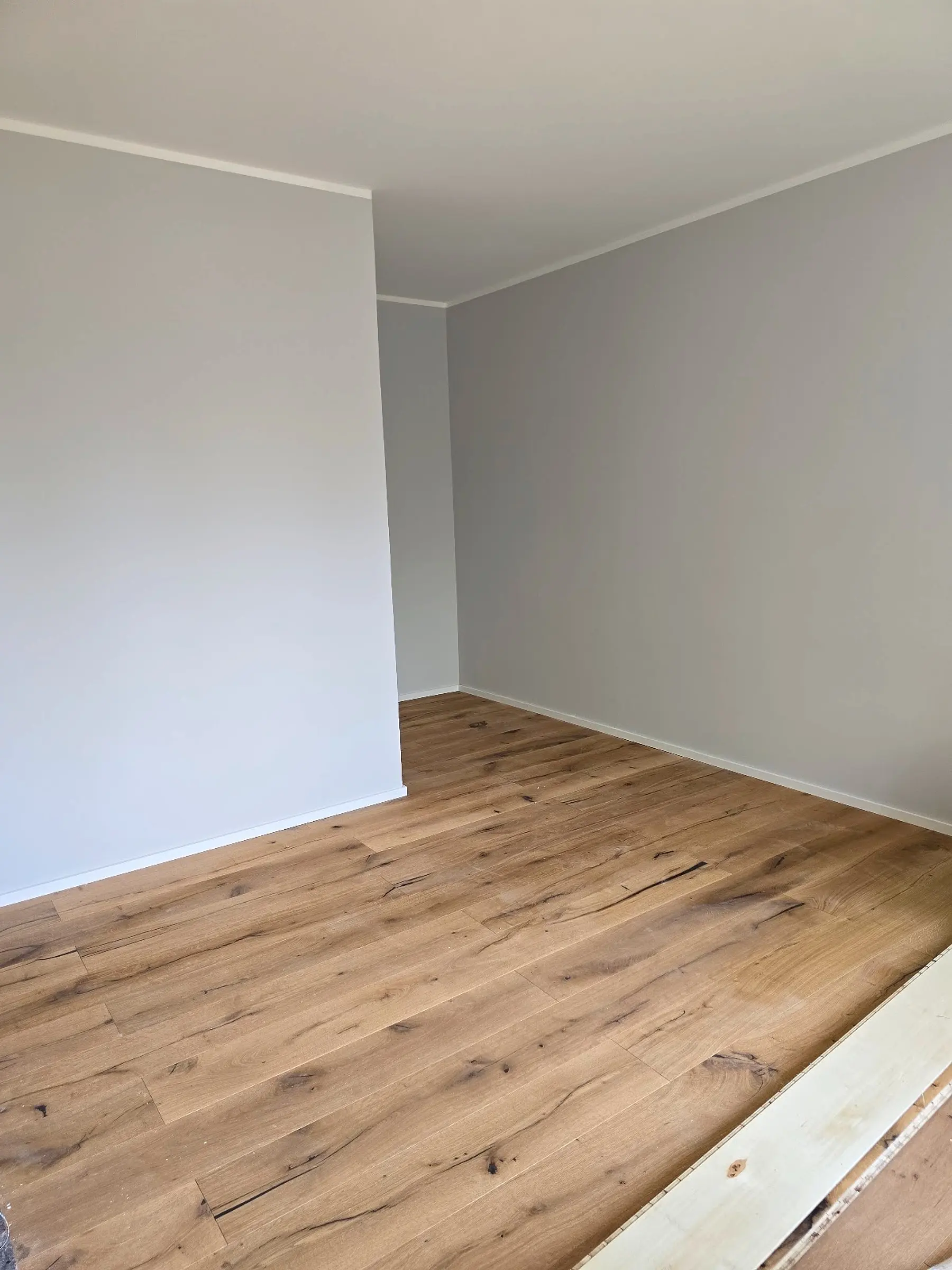 Leerer Raum mit frisch verlegtem Holzboden und weiß gestrichenen Wänden