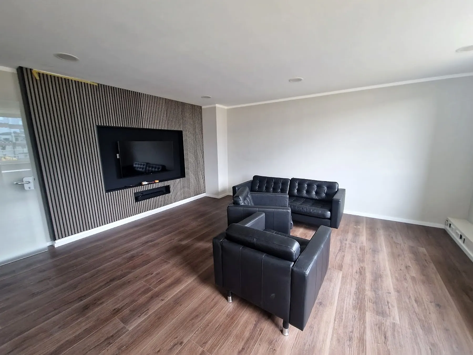 Wohnzimmer mit dunkler Lamellenwand, Holzboden und hellem Anstrich