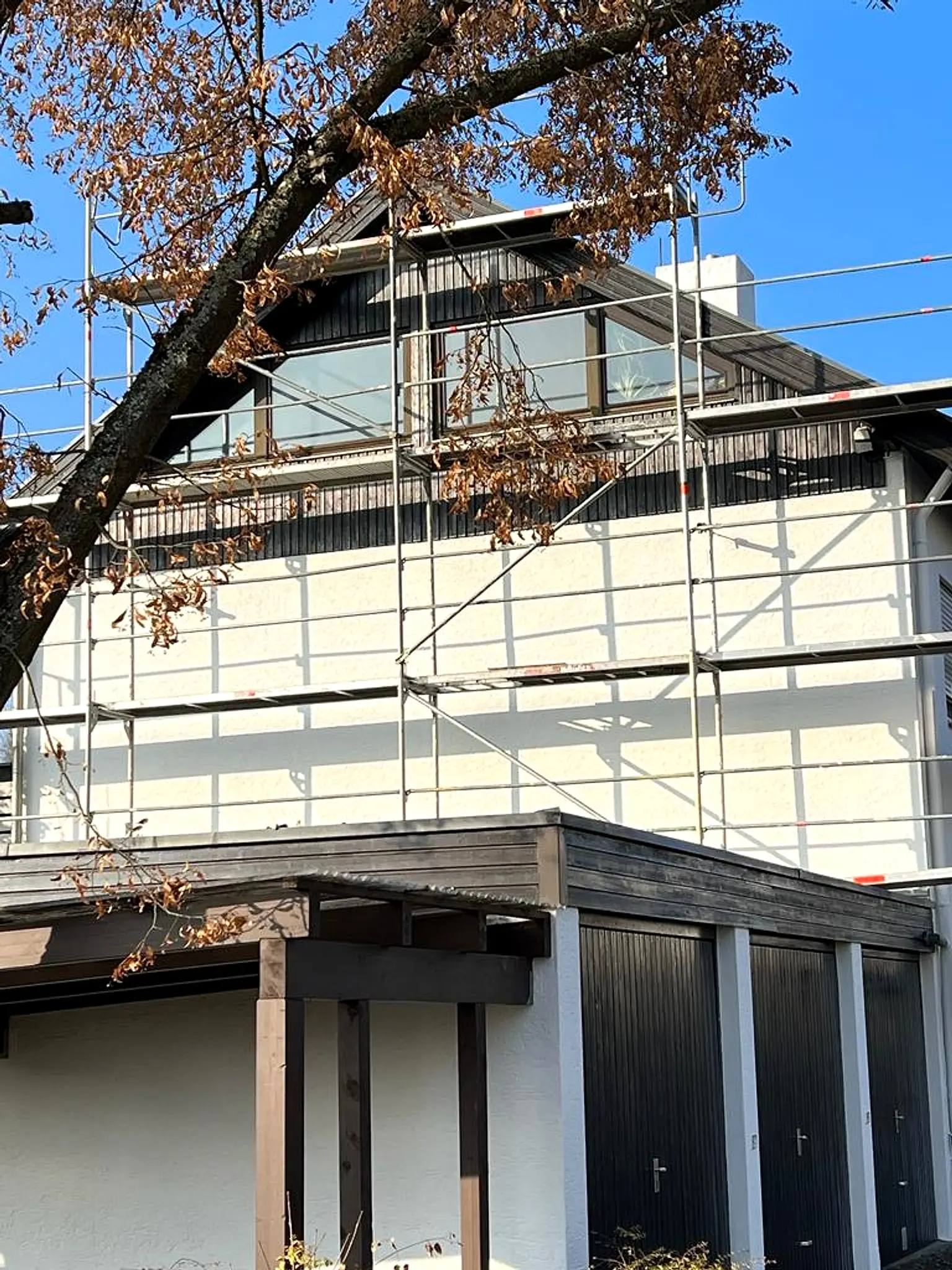 Eingerüstetes Wohnhaus mit weißer Fassade, davor ein Baum